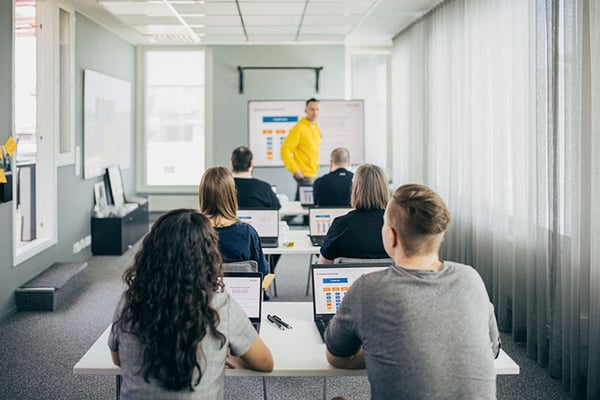 A picture of people sitting in a classroom withe their laptops following a presentation held by an Eficode representative.