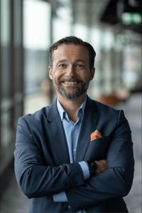 A picture of Jens Skyman, Leader for the Nordic region at HashiCorp, crossing his hands and smiling while wearing a navy blue suit jacket and a blue dress shirt with an orange pocket square.